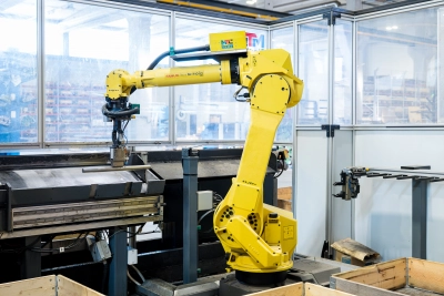 Teollisuusrobotti käsittelee metallikappaletta tuotantolinjalla. Kuvassa näkyy automatisoitu työvaihe Stén-konsernin tuotantoympäristössä, jossa panostetaan laatuun, tehokkuuteen ja prosessien kehittämiseen.