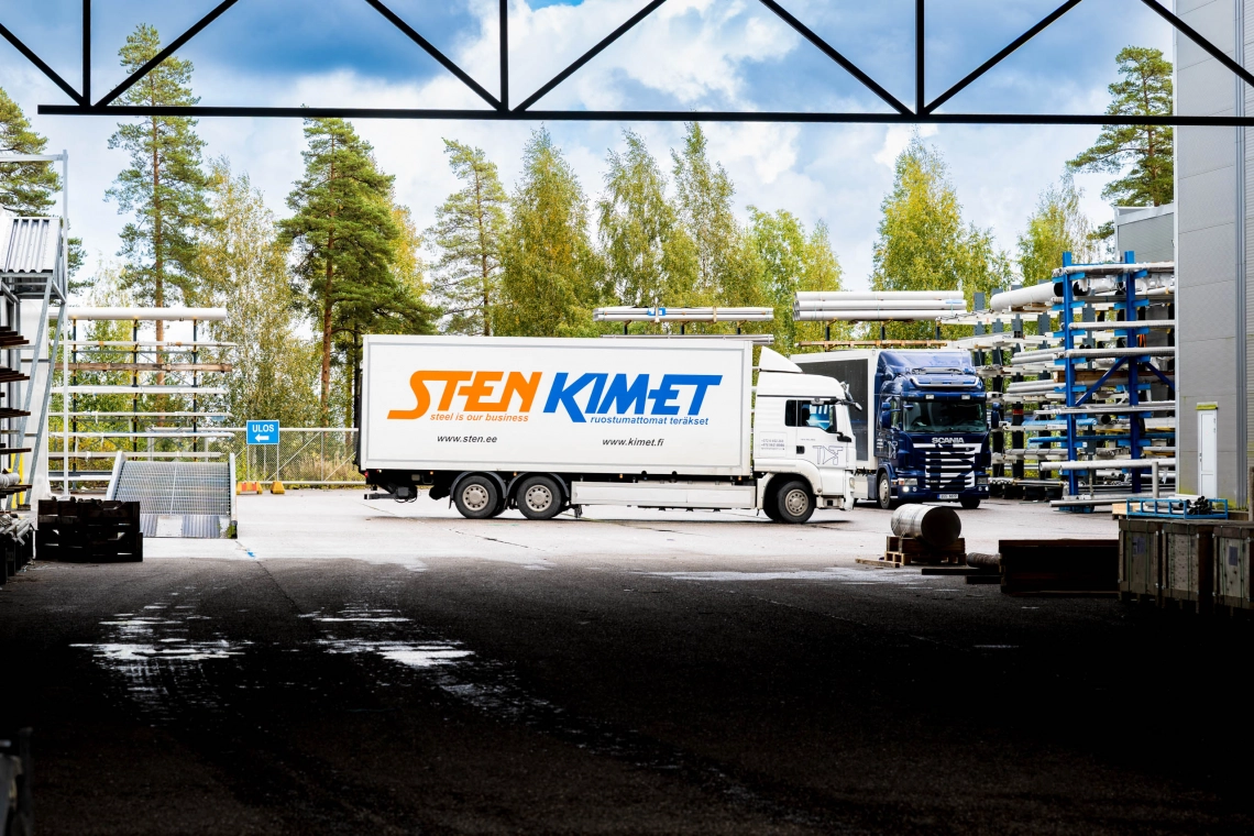 tee alt kuva teksi Sten Teräksen ja Kimetin logoilla varustettu kuorma-auto teräspalvelukeskuksen piha-alueella Nurmijärvellä. Taustalla teräsvarasto ja toinen kuorma-auto.
